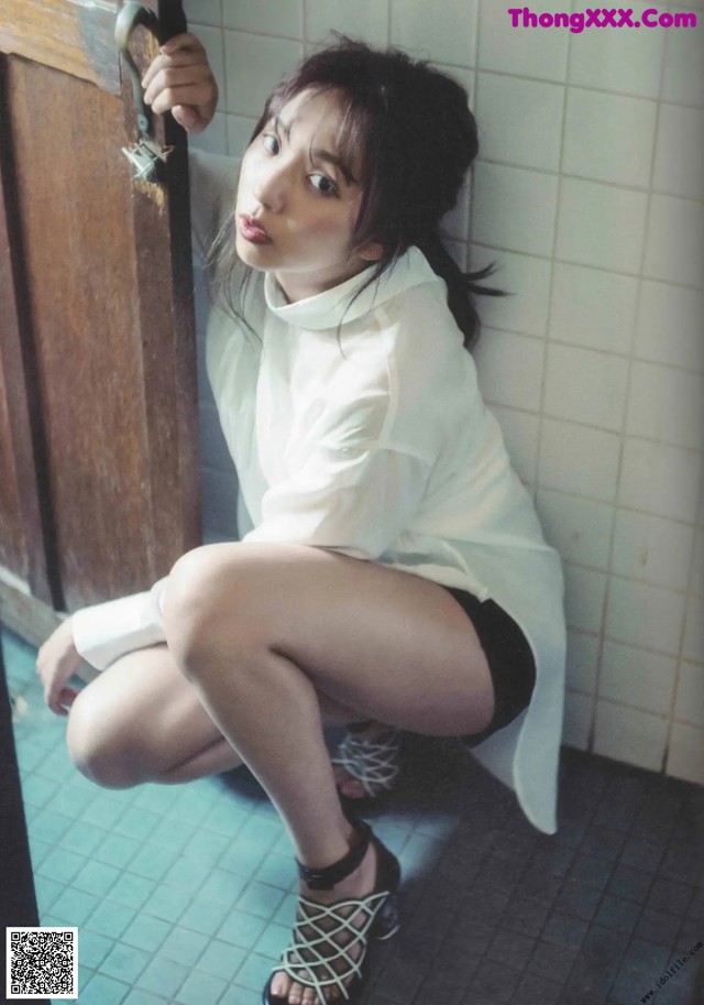 A woman in a white shirt and black shorts leaning against a door.