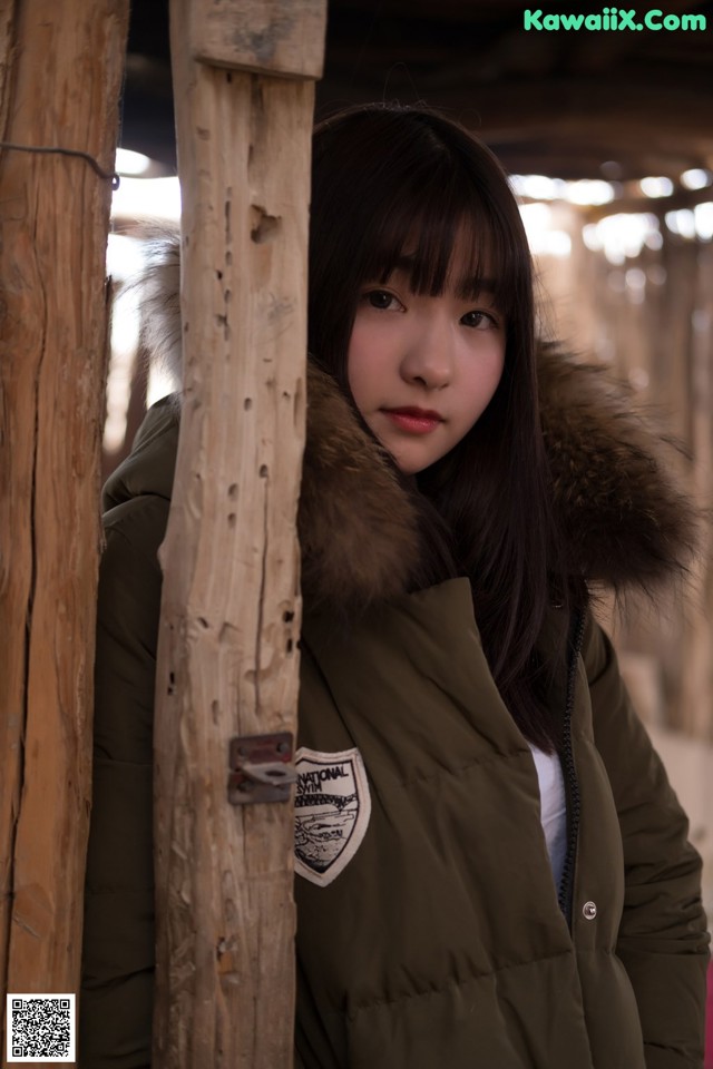 A woman in a green jacket leaning against a wooden pole.