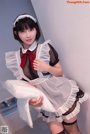 A woman in a black and white maid outfit leaning against a wall.