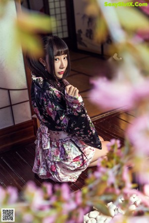 A woman in a kimono sitting on the floor with her legs crossed.