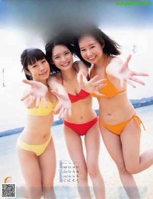 A group of three women in bikinis standing on a beach.