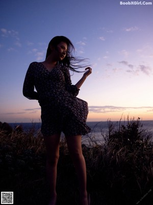 A woman in a purple dress holding a bunch of tall grass.