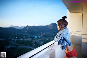 A woman in a red bikini and a denim jacket posing on a balcony.