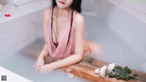 A woman in a pink lingerie sitting in a bathtub.