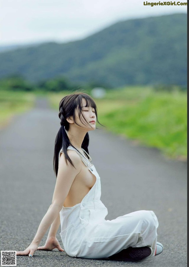 A woman in a white dress sitting on the side of a road.