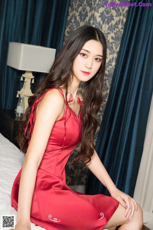 A woman in a red dress sitting on a bed.