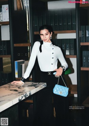 A woman standing in front of a desk holding a handbag.