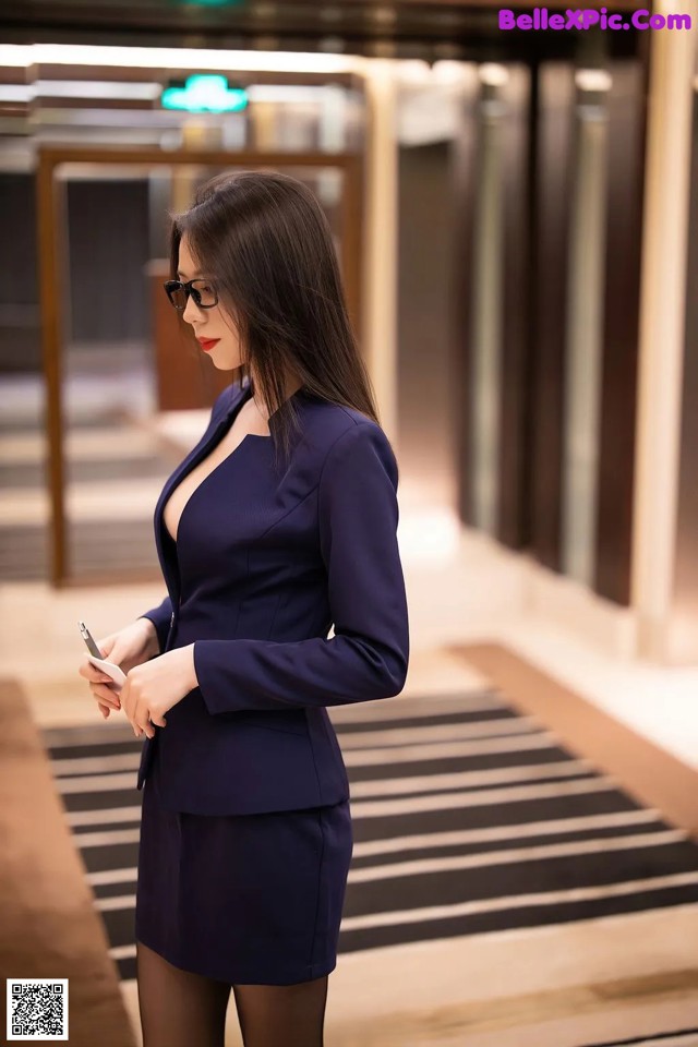 A woman in a blue suit is looking at her phone.