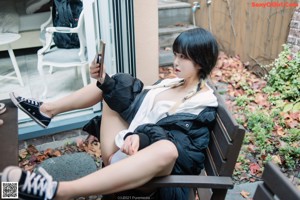 A woman in a black jacket and white thong crouching on a rock.