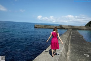 A woman in a pink dress is walking on a puddle of water.